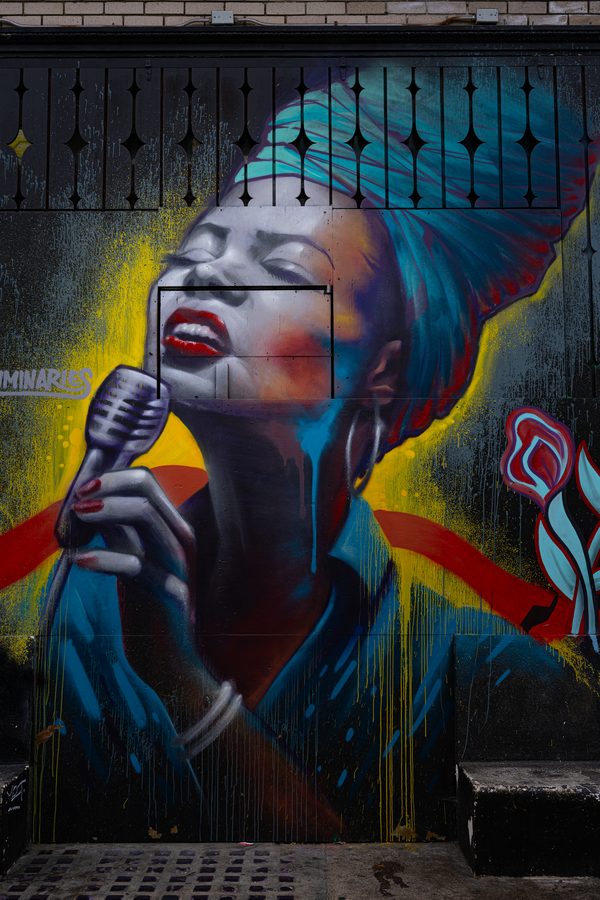 Fresque de street art à San Francisco : chanteuse de jazz aux yeux fermés tenant un micro, turban bleu, lèvres rouges, coulures jaunes sur fond noir