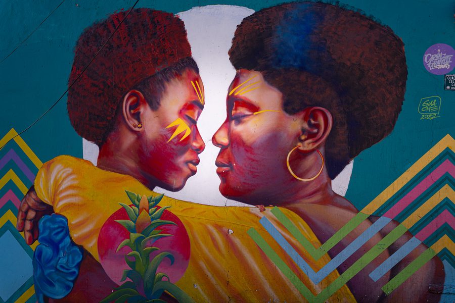 Fresque de street art à Bogotá : deux visages de femmes front contre front, peintures jaunes sur les joues, fond turquoise et motifs en chevrons